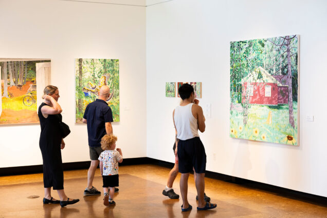 Photo: A picture of people looking at a painting of a house surrounded by greenery during an art installation