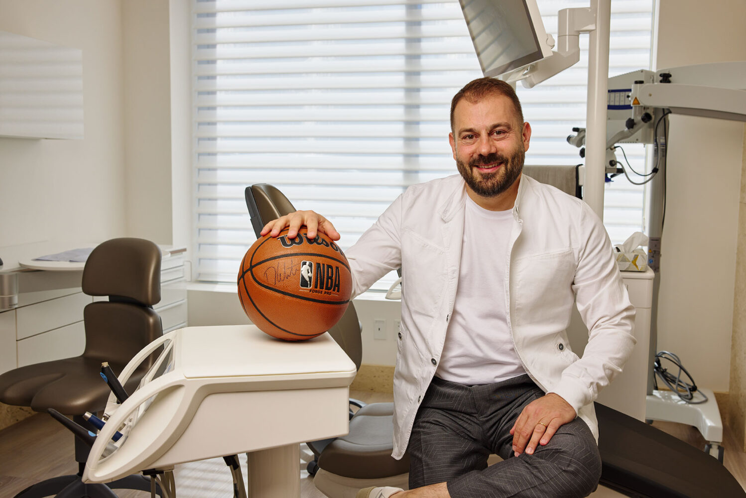 Photo: A picture of a dentist in a white coat smiling and posing with a basketball in his dental office