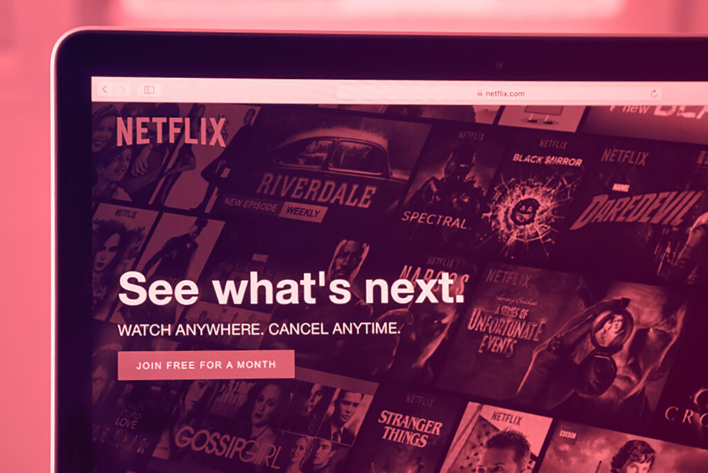 Image: A shot of a laptop screen with the Netflix site loaded in full screen. The image has a pink overlay over the image.