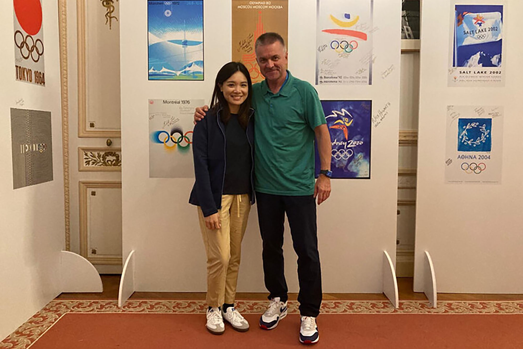 Photo: A young women< Karen Lo, with a older Olympian, Peter Haberl, stand together, arm around shoulders and smile for the photo.