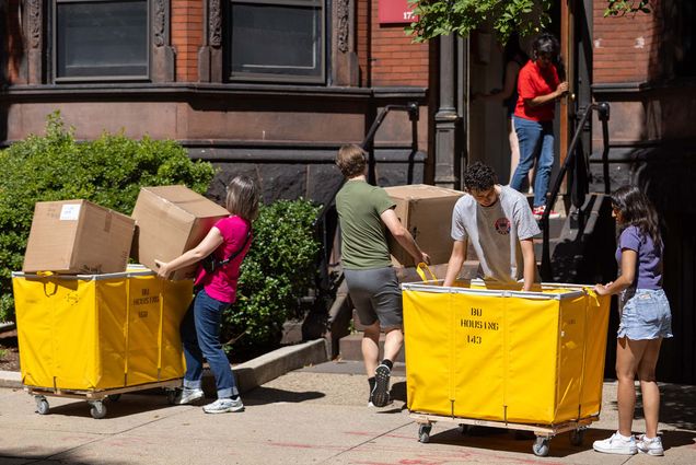 Photo: A picture of people moving items into a brick, BU dorm building using large, yellow rolling bins with "BU Housing" on the side.