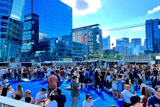 Photo: A picture of Cisco, an outdoor beer garden in Boston. It is full of people standing with beverages and surrounded by large skyscrapers