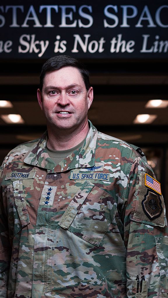 Photo: A man in a military outfit with badges and stars indicating he is a General in the US Space Force. The Banner above his head reads "United States Space Force. The Sky is Not The Limit"