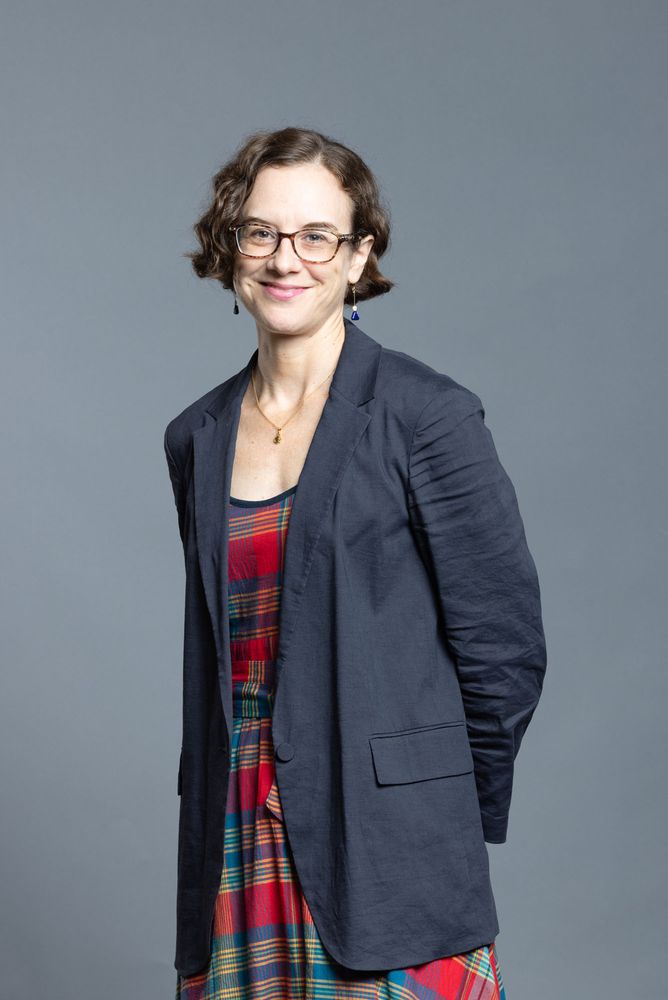 Photo: A white women with short brown hair and a gray blazer and square glasses.