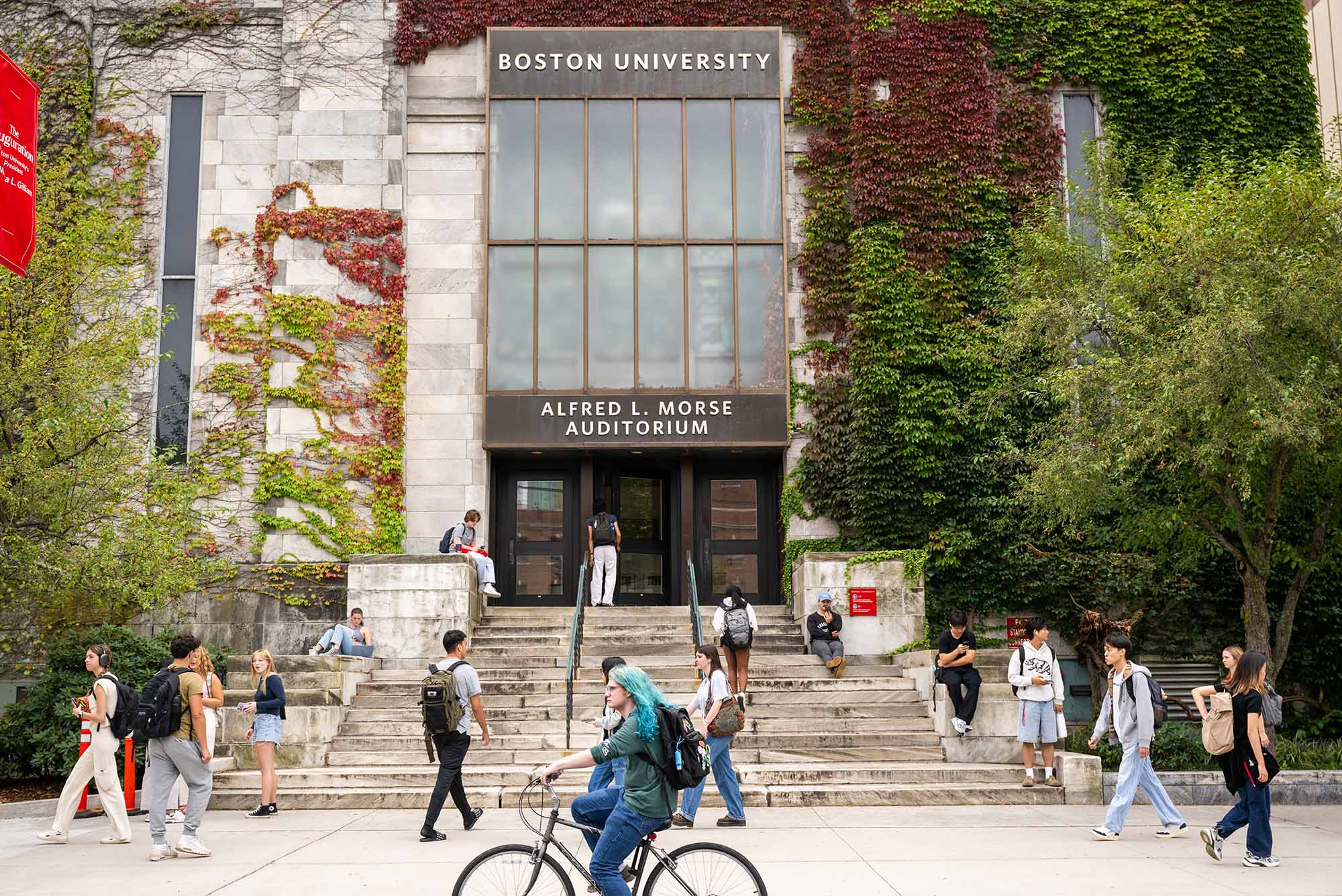 Photo: The exterior of Boston University's Alfred L. Morse Auditorium. The building is made of stone and covered in autumnal colored foliage, with many people gathered around its steps and along the street