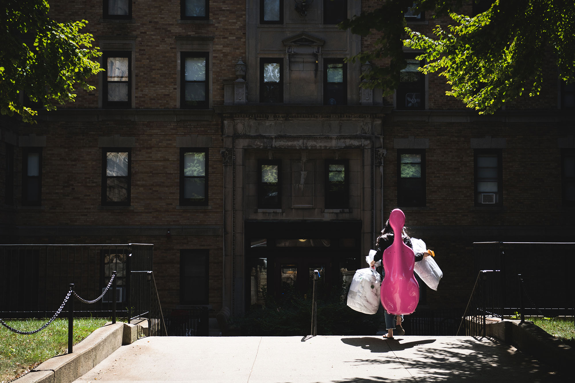 Photo: A student carrying a pink cello case on her back as she moves into a BU dorm building