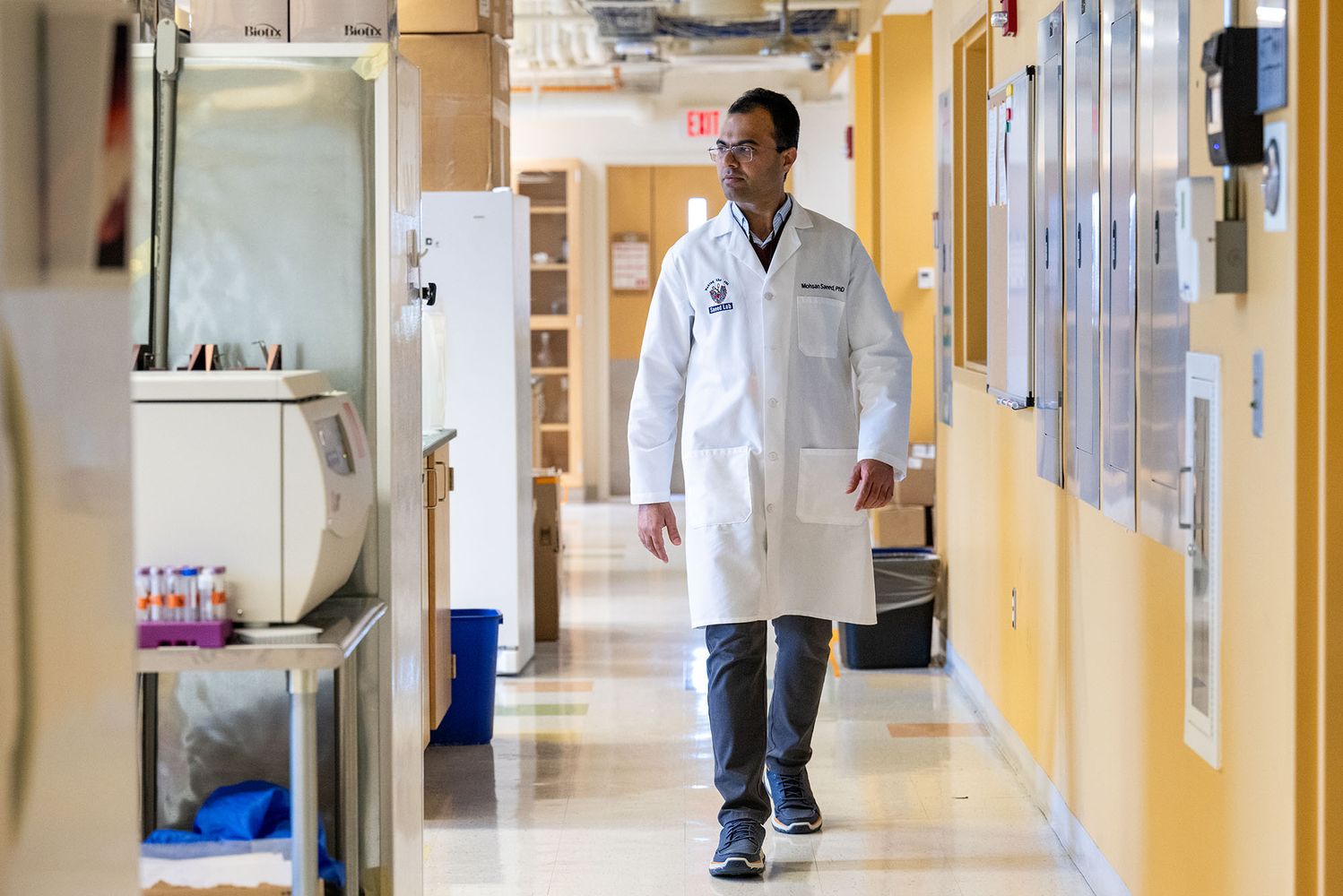 Photo: A man in a labcoat walking down a lab corridor