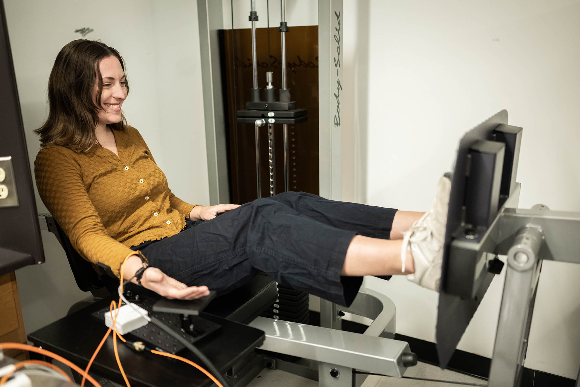 Ph.D Candidate, Ariane Garrett demonstrates how to use a cuff-less blood pressure monitor while she uses a leg press machine.