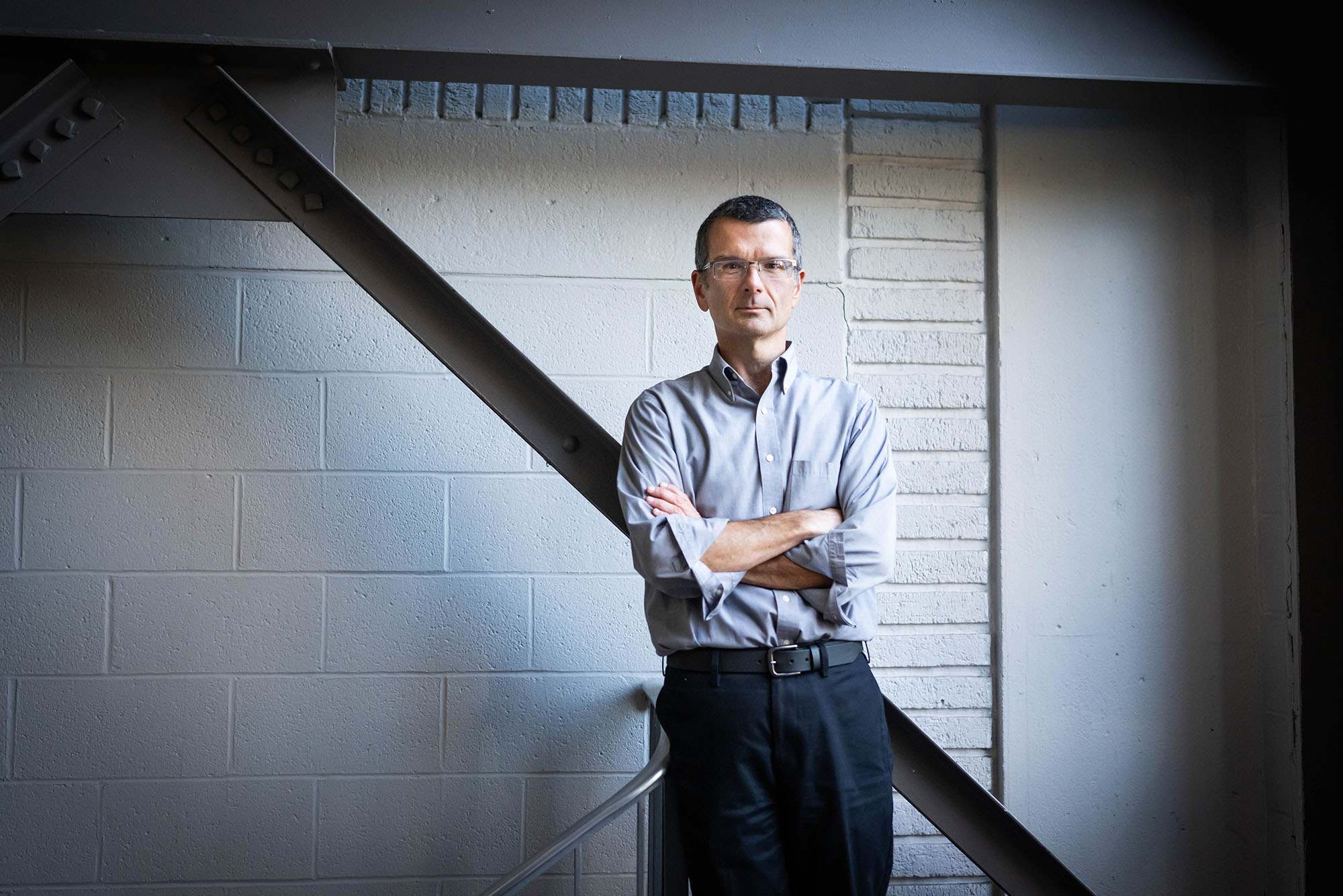 Photo: A man in a long-sleeve button down crossing his arms and leaning back. He has a very short haircut and glasses