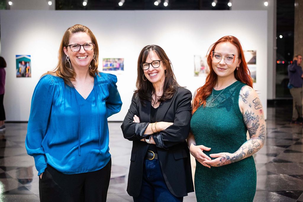 Photo: Three women posing and smiling at a gallery exhibit