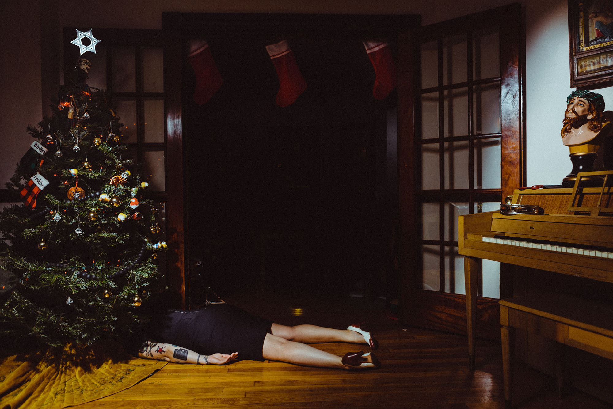 Photo: A woman lying facedown under a Christmas tree in a decorated living room
