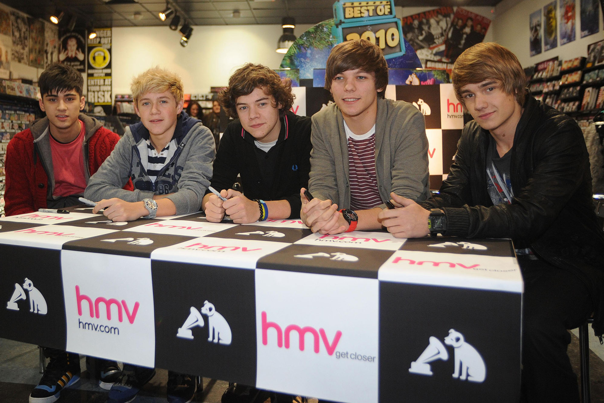 Photo: Zayn Malik (from left), Niall Horan, Harry Styles, Louis Tomlinson, and Liam Payne of One Direction sitting behind a table that says "hmv" on the front