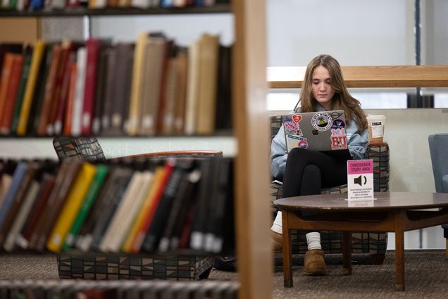 Photo: A BU student studying in Mugar Library with a stack of books in the foreground
