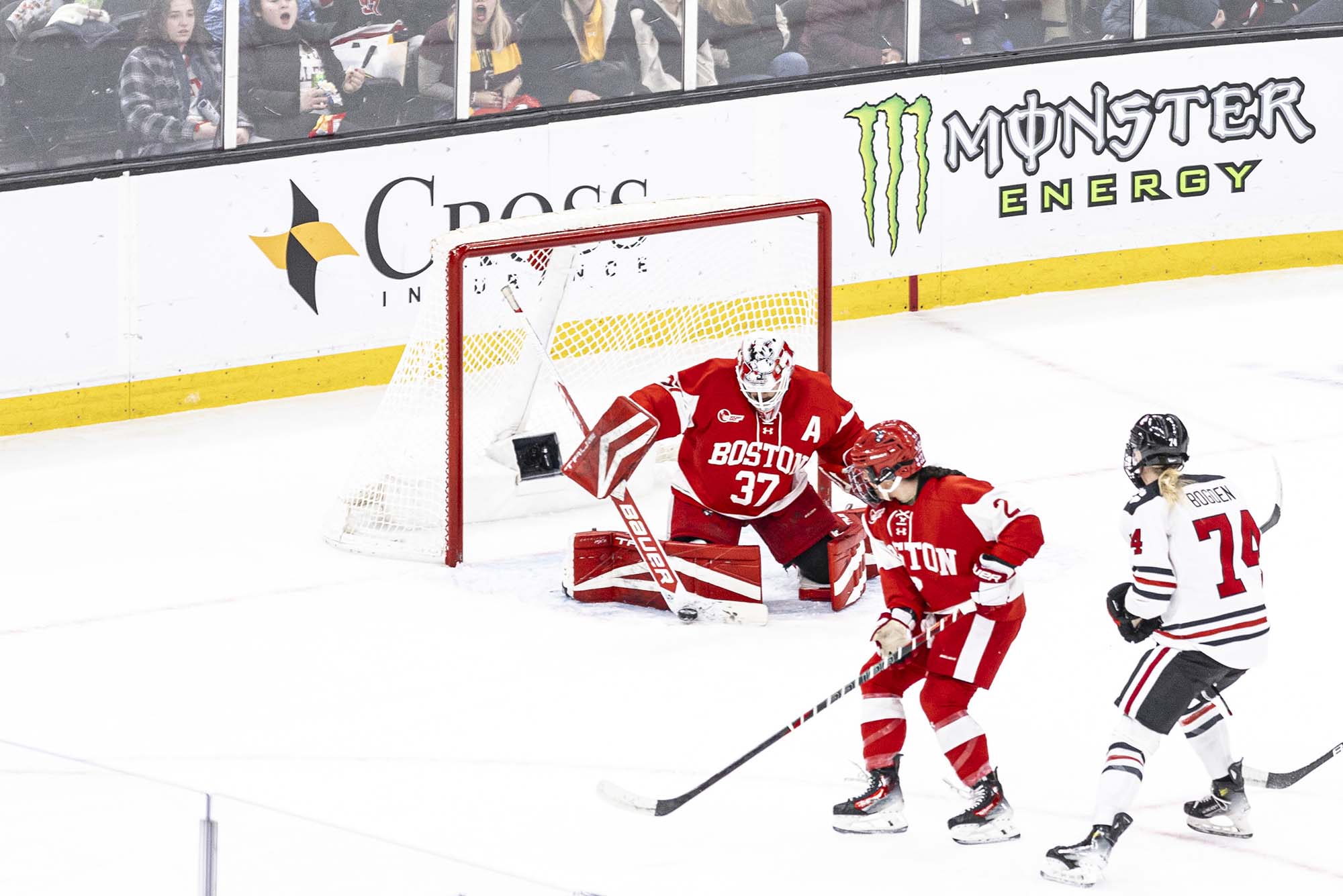 Photo: A BU hockey player, a Northeastern hockey player, and the BU women's hockey player on the ice, in the midst of a play.