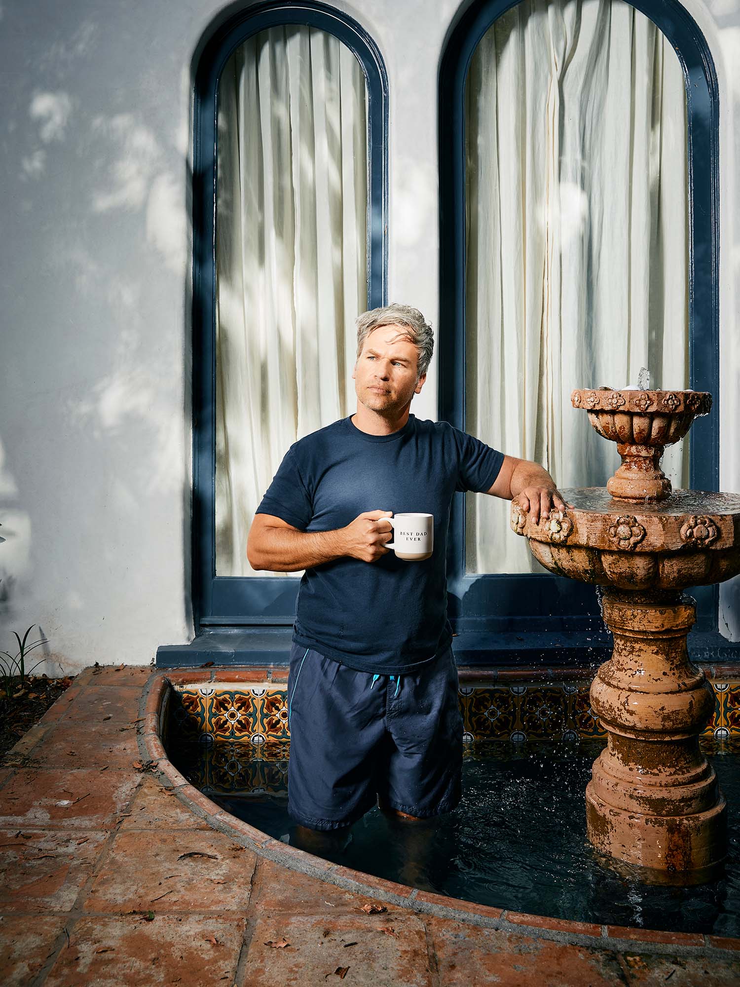 Photo: A man with gray hair wearing a blue tshirt, holding a coffee mug, and standing inside a fountain