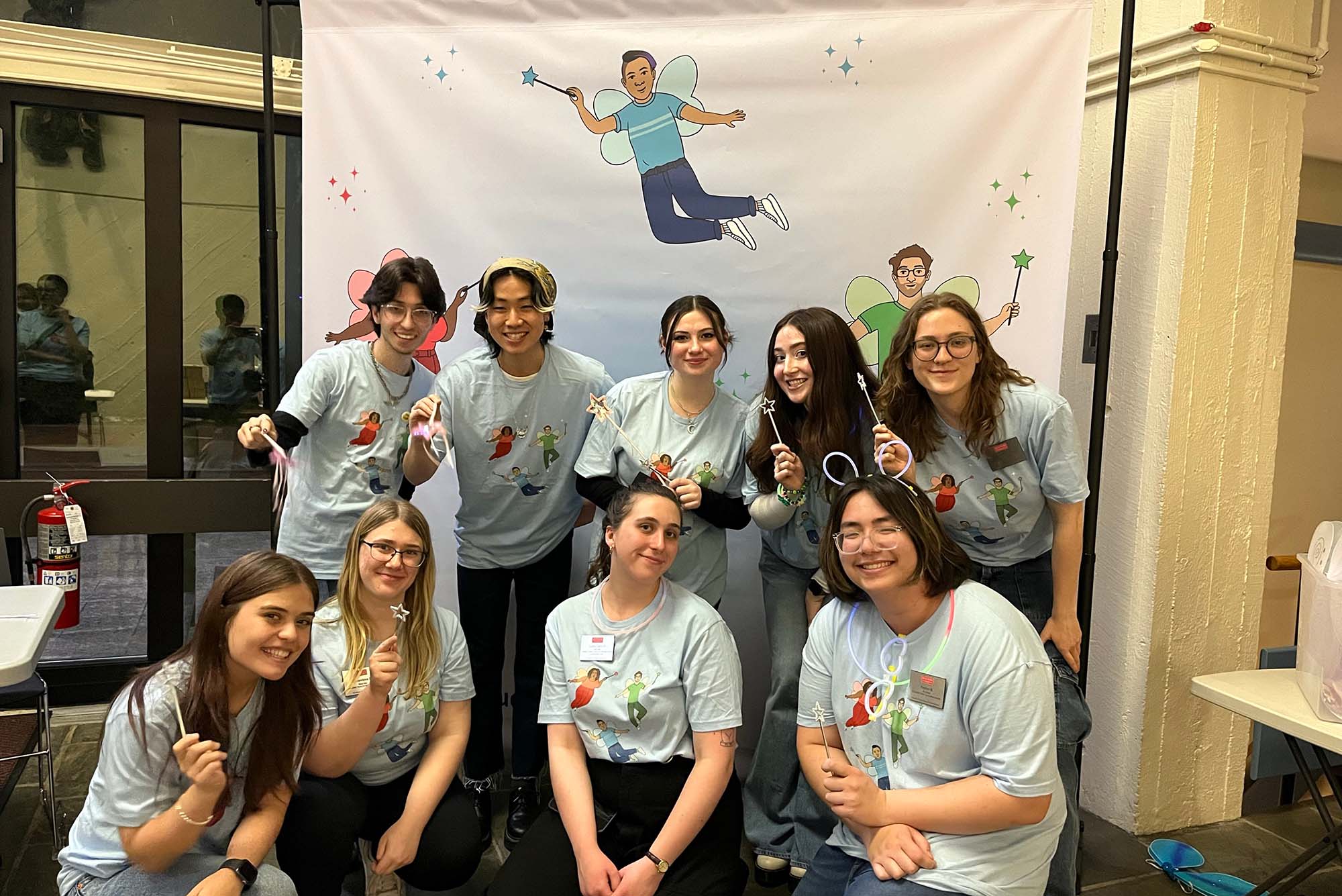 Photo: A group of BU students posing with wands in front of a Condom Fairy banner