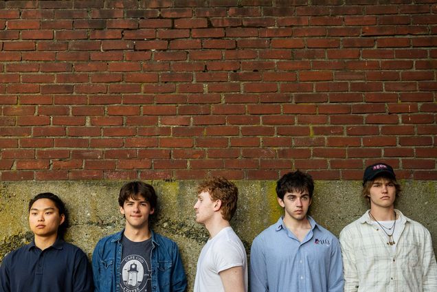 Photo: A band of 5 male members lined up and posing in front of a brick wall