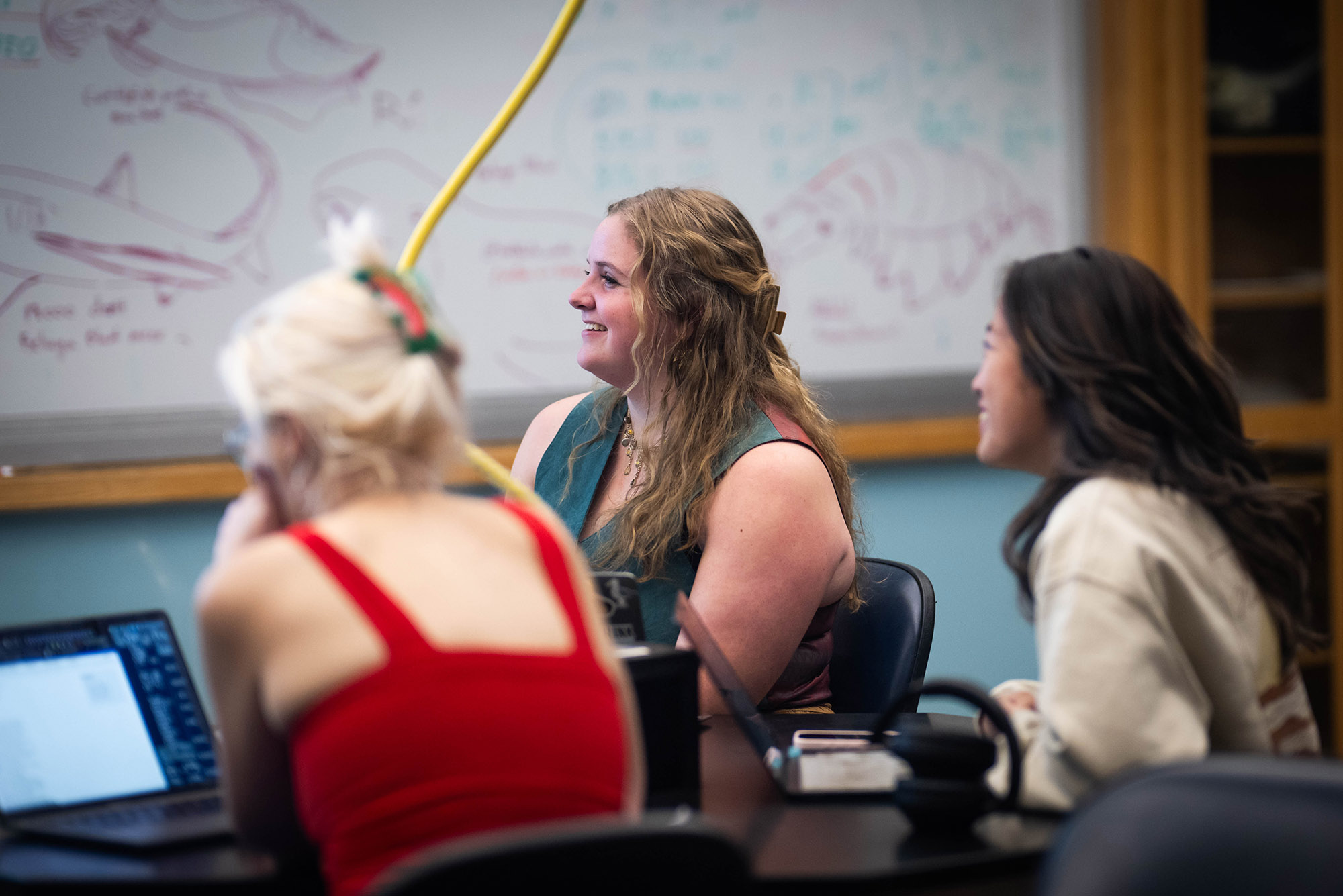 Photo: A young white woman with long mousy brown hair sits in a classroom attentively.