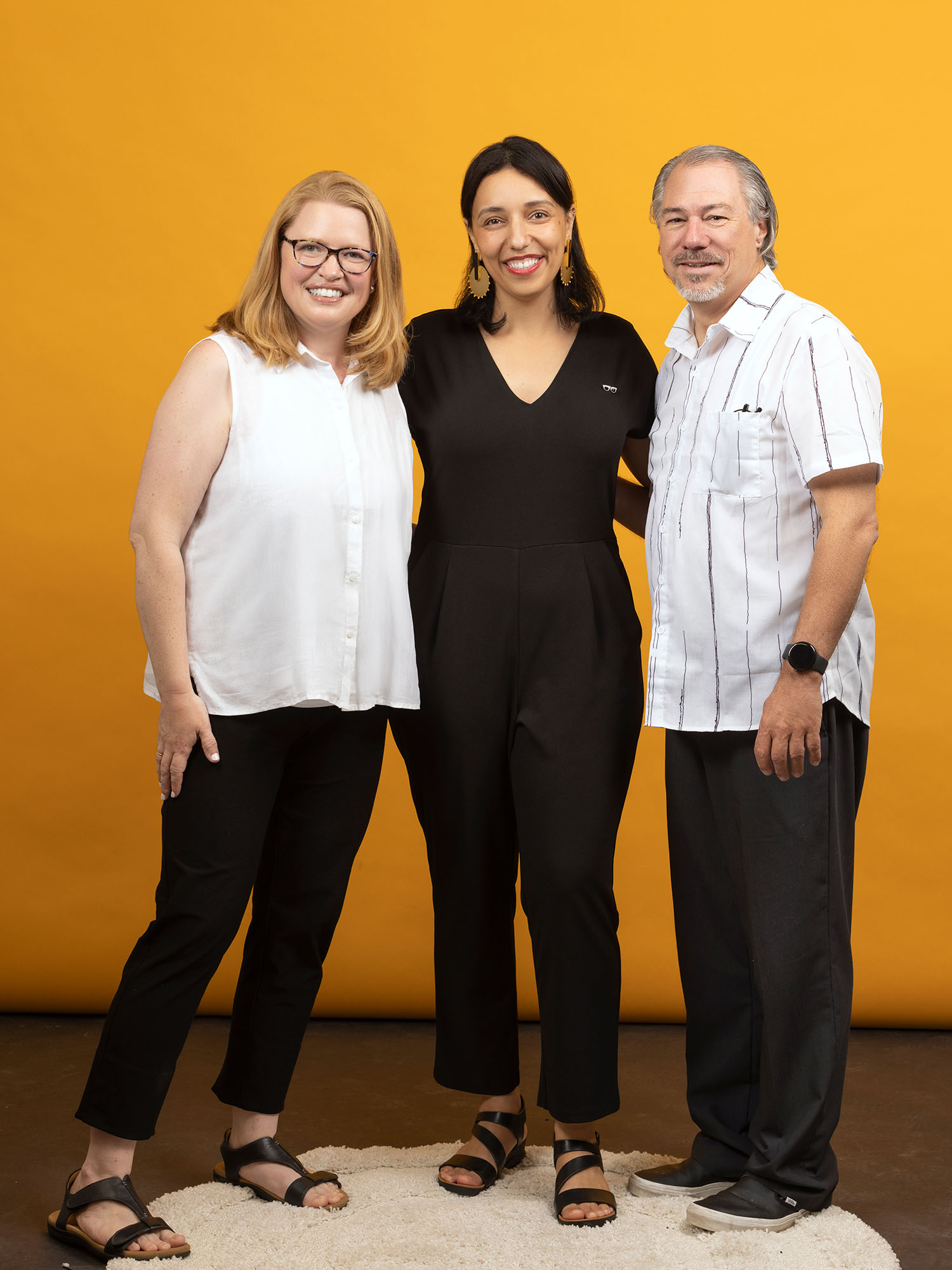 Photo: Three people standing and posing with smiles in front of a yellow background