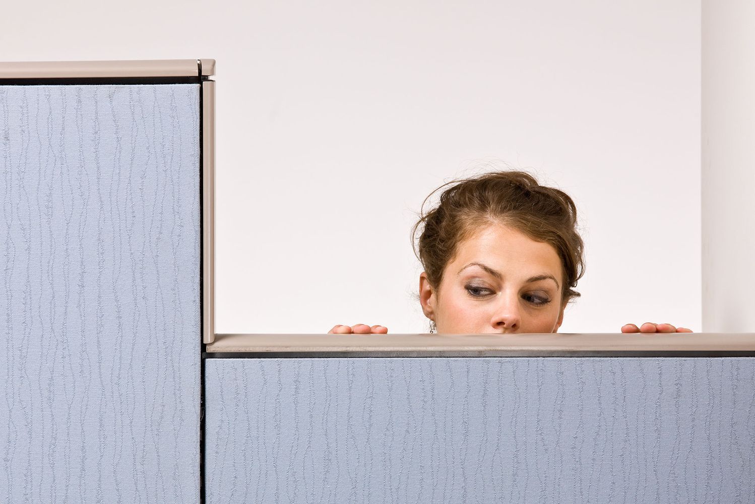 Photo: A businesswoman peering over cubicle wall