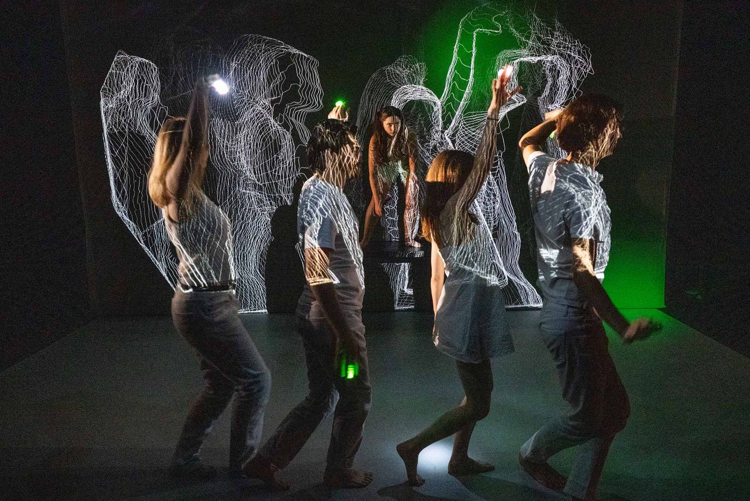 Photo: Four actors walk in a line underneath a wavy laser light display