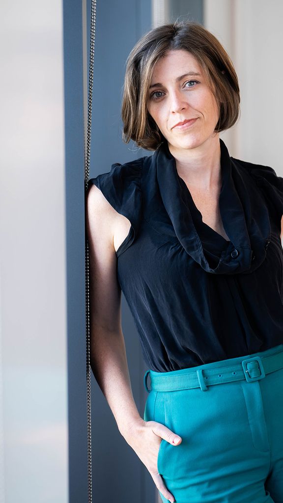 Photo: A woman with short hair leans against a blue wall in this posed formal portrait