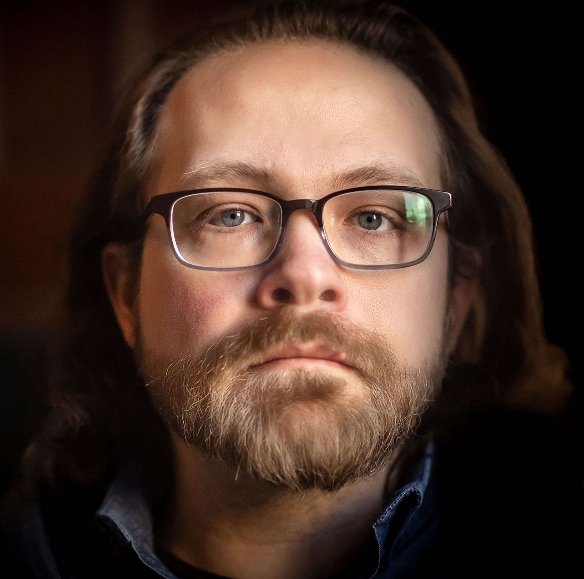 Photo: A portrait image of a white man with long mousy blonde hair and a full beard wearing wire frames