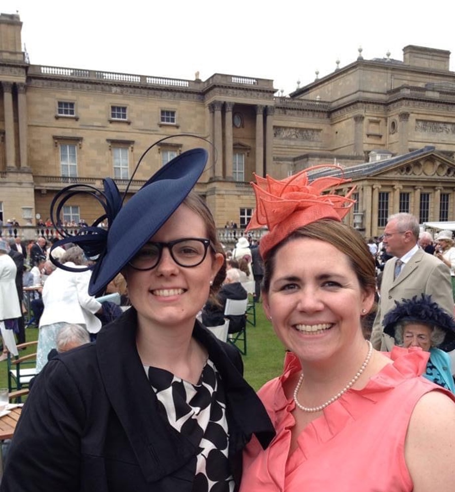 Photo: Lamontagne (right) smiles at a garden party with a friend. She wears an all pastel pink outfit with a small hat on top of her brown hair. Her friend, on the left and in all black with a black and white blouse. She wears a black hat, similar to Lamontagne and black glasses.