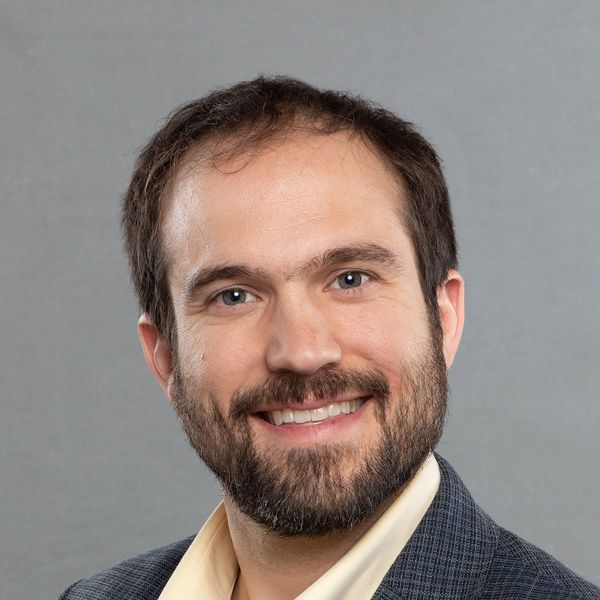 headshot portrait of C. Ian Stevenson, smiling. He is wearing a suit jacket and collared dress shirt.