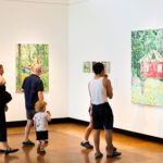 Photo: A picture of people looking at a painting of a house surrounded by greenery during an art installation