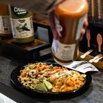 Photo: Someone holding a sauce bottle pours the contents on their plate of food.