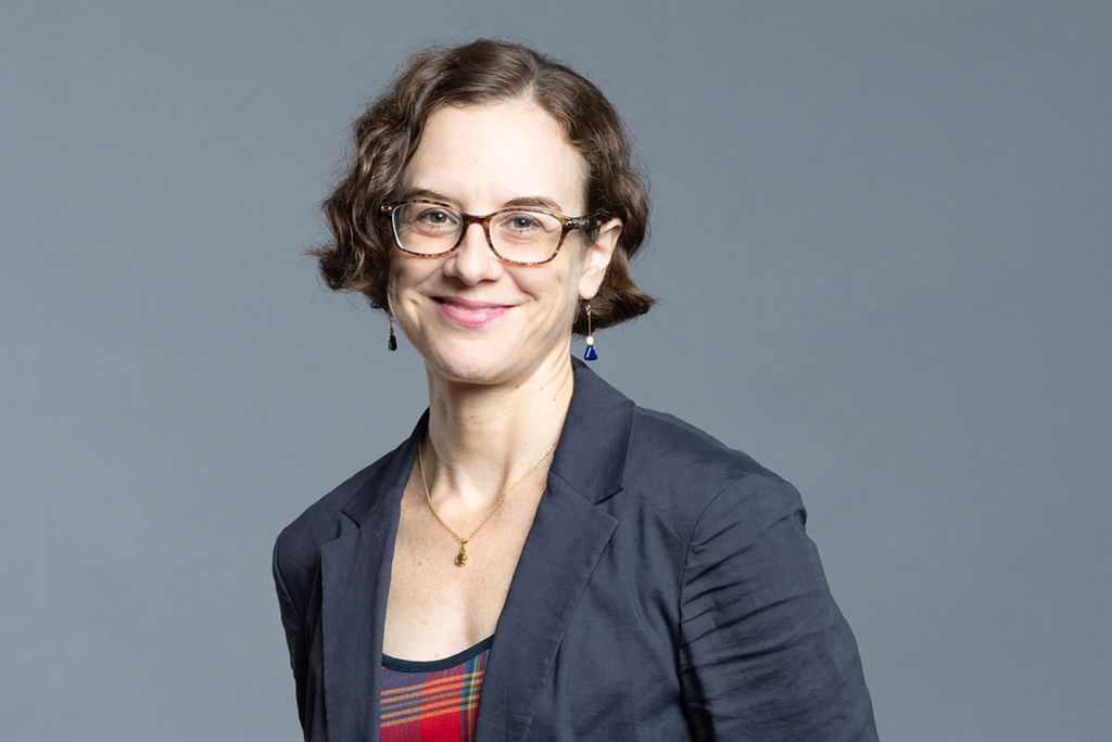 Photo: A white women with short brown hair and a gray blazer and square glasses.