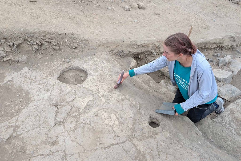 Photo: A white woman crouched down to dust of archaeological findings on the ground.