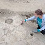 Photo: A white woman crouched down to dust of archaeological findings on the ground.