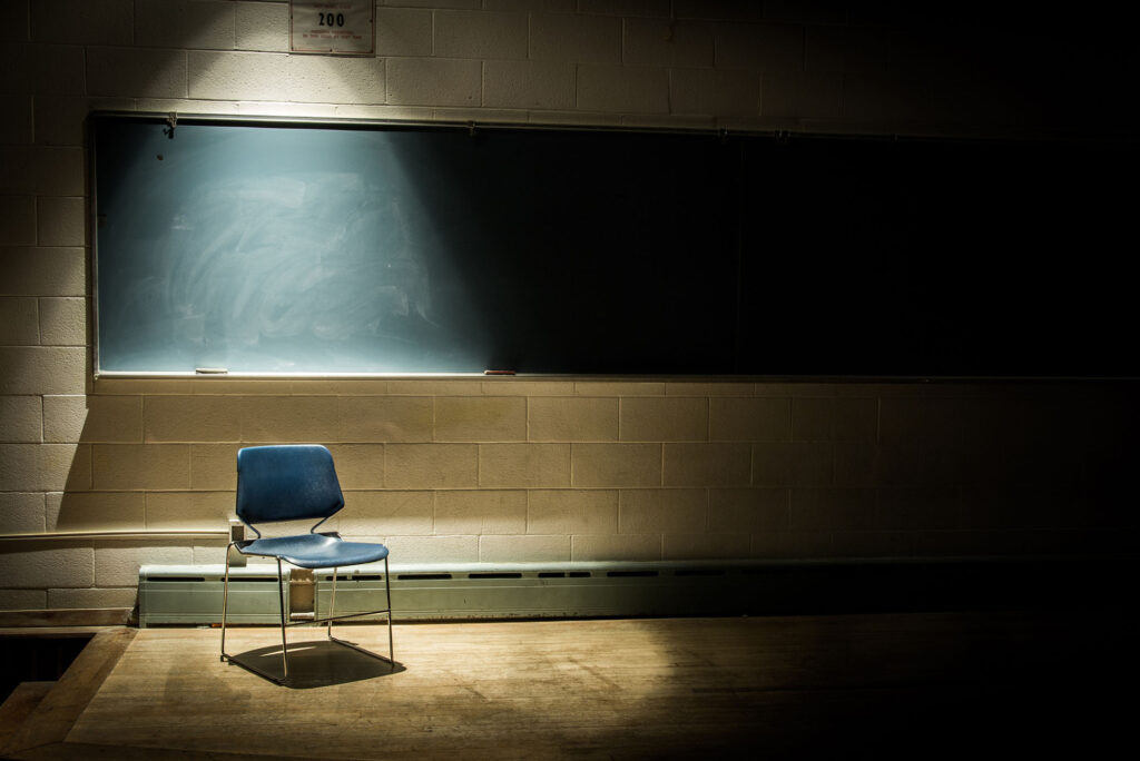 Photo: A picture of a dark classroom with a spotlight on the single chair in the room