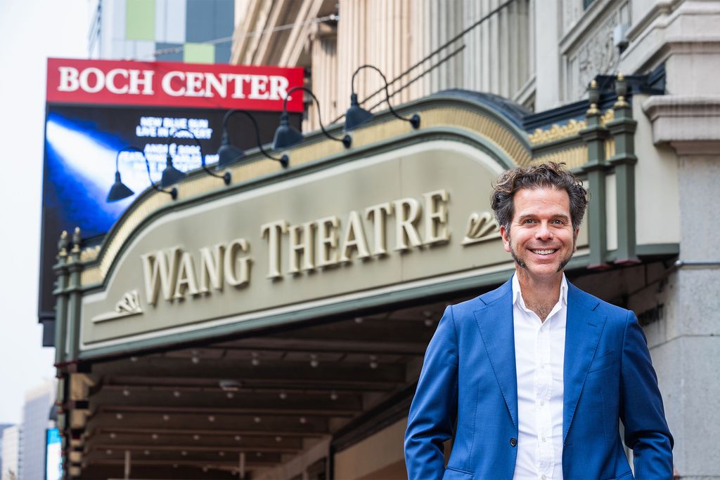 Photo: A Man in a blue suit stands under a marquee reading "Wang Theatre"