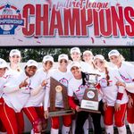 Photo: Boston University's Softball Team holding two large trophies under a banner that reads "Champions"