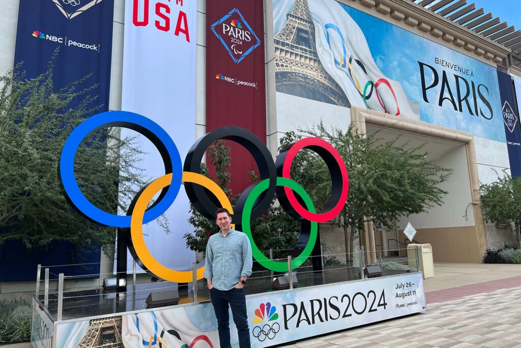 Photo: A man in business casual dress standing in front of the Olympic Rings in Paris for the 2024 Summer Olympic Games