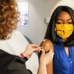 Photo: A black woman receives a band aid from a healthcare provider after receiving the COVID vaccine