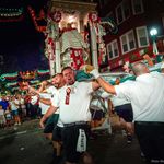 Photo of the St. Agrippina’s Feast celebration. A group of men hoist an ornate statue as the parade and shout during the night in the North End street.