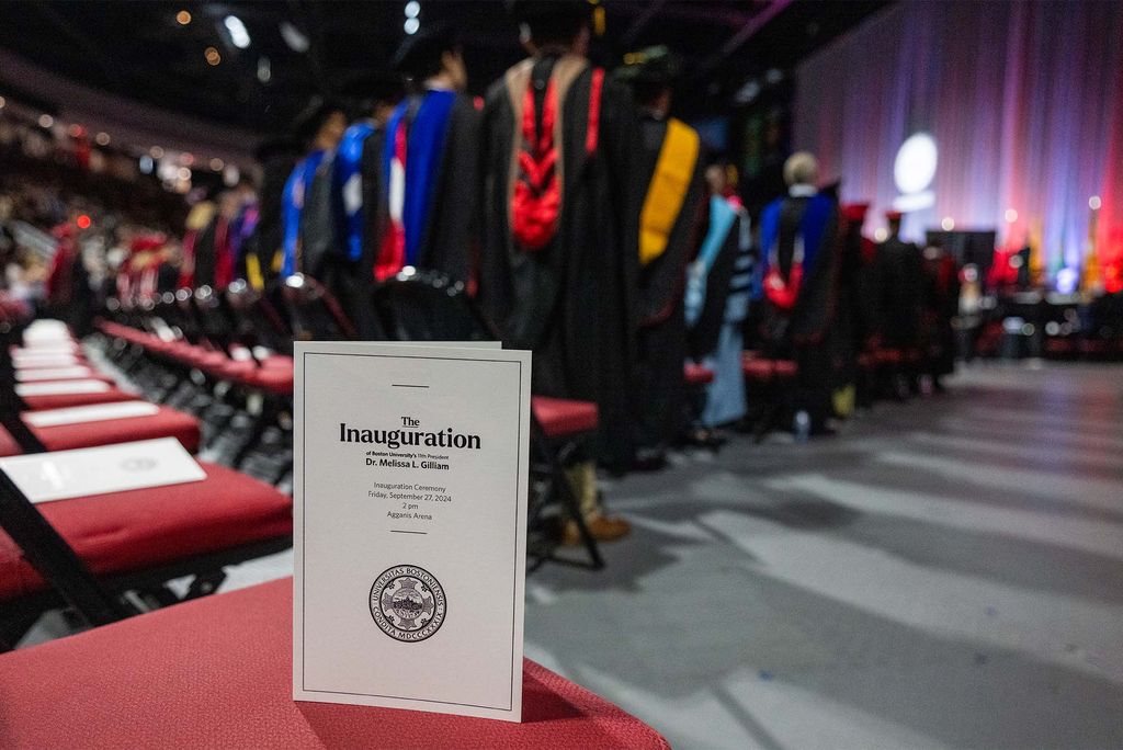 Photo: Program for Melissa L Gilliam's inauguration at BU's 11th President in September 2024, sitting on a chair at the event as the crowd applauds