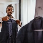 Photo: Young black man putting on a black formal vest