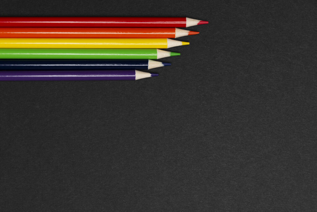 Photo: Pencils in row made of rainbow flag colors symbolizing LGBT movement on black background.