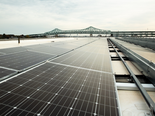 Rooftop solar panels on top of a building with the Tobin Bridge and Charlestown, MA, United States in the background.