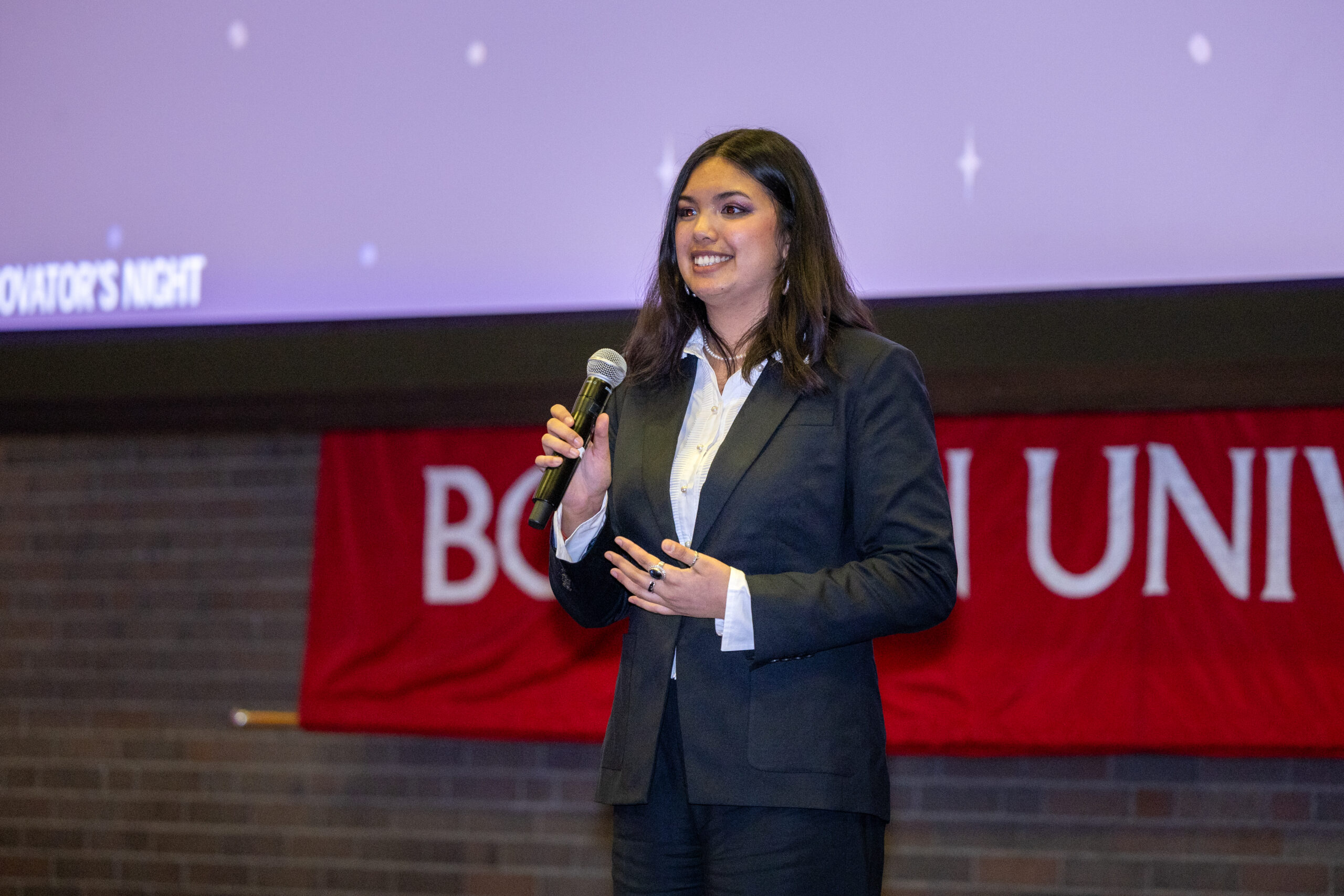 A woman speaks into a microphone on stage in front of a Boston University banner