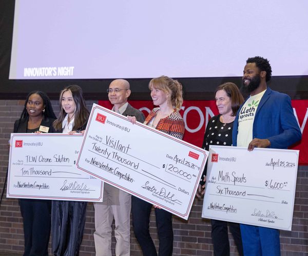 Group of student founders holding prize money checks on stage at an event