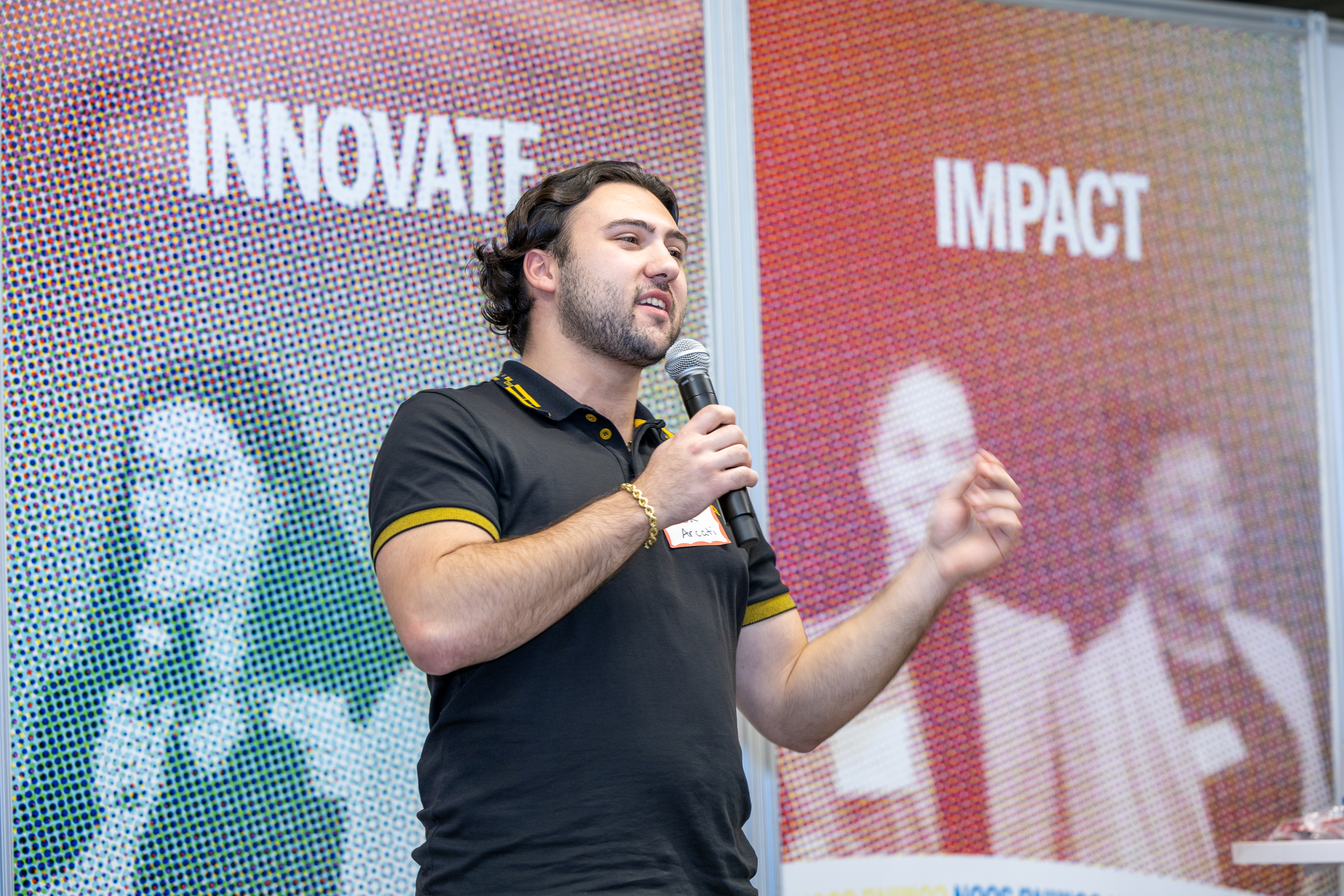 Man with a microphone speaks at an event in front of a colorful backdrop