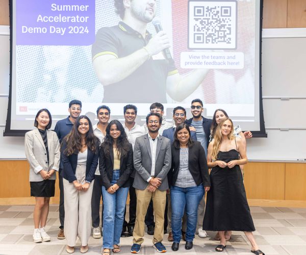 Cohort of student founders posing on stage for a group photo in front of projector screen