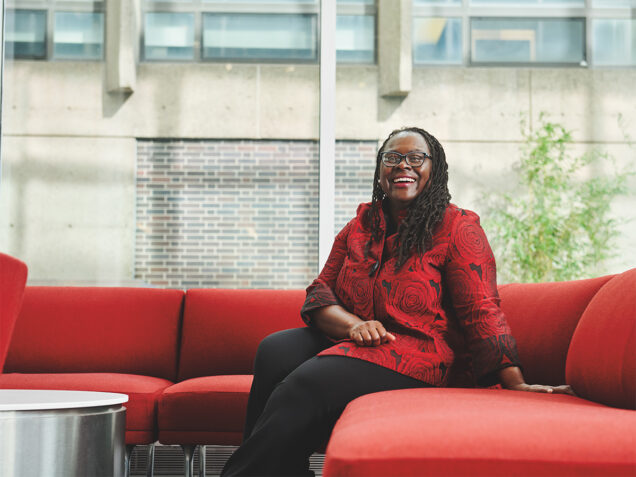 Dean Angela Onwuachi-Willig sits on a red couch, smiling, in the Butler atrium at BU Law
