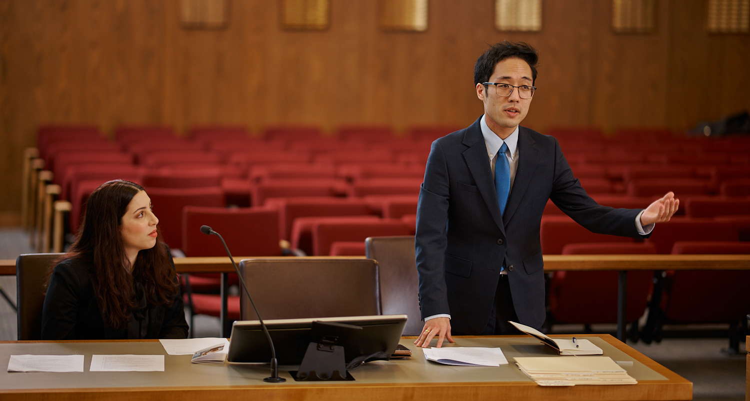 Two students in business attire present a case in a practice courtroom.
